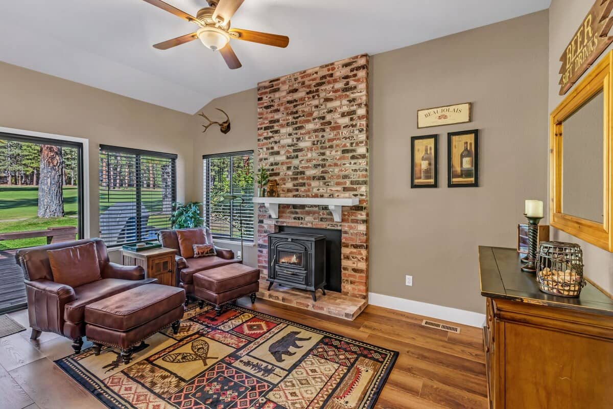 Living room with a floor-to-ceiling brick fireplace and wood stove, leather chairs and fairway views at 119 Cottonwood, Plumas Pines — 3-bedroom Plumas Pines vacation rental in Graeagle, CA