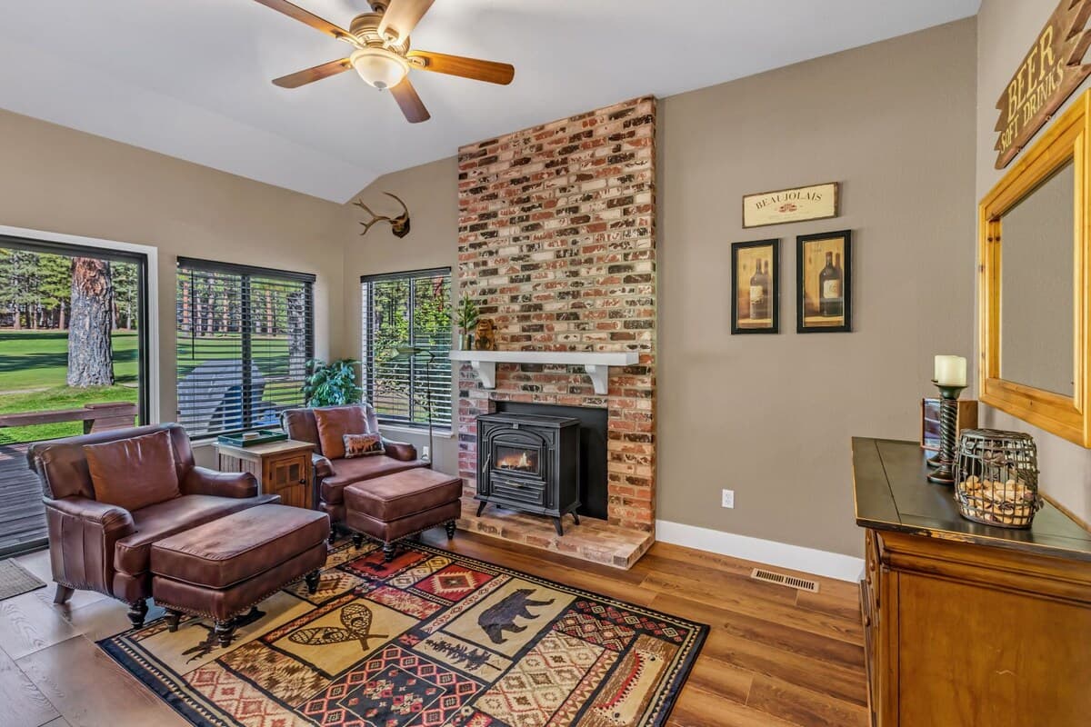 Living room with a floor-to-ceiling brick fireplace and wood stove, leather chairs and fairway views at 119 Cottonwood, Plumas Pines — 3-bedroom Plumas Pines vacation rental in Graeagle, CA