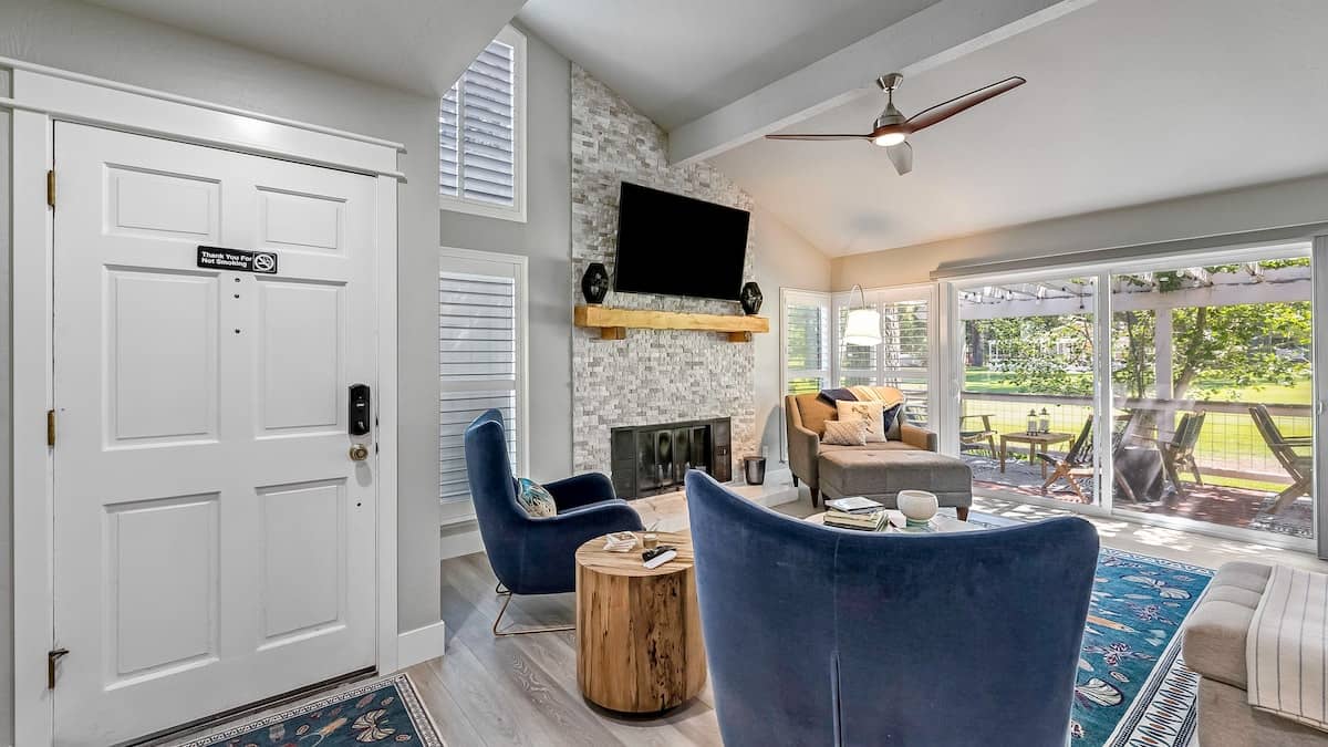Living room with a stacked-stone fireplace, wall-mounted TV, navy velvet armchairs and sliders onto the deck and lawn at 37 Aspen, Plumas Pines — 4-bedroom Plumas Pines vacation rental in Graeagle, CA