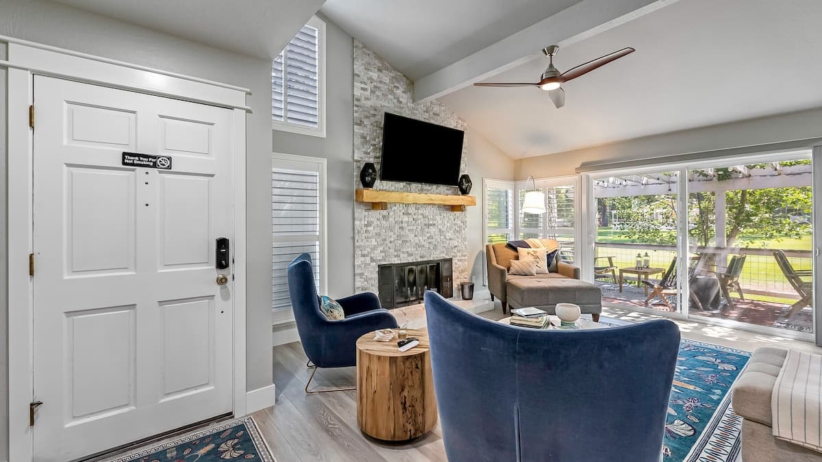 Living room with a stacked-stone fireplace, wall-mounted TV, navy velvet armchairs and sliders onto the deck and lawn at 37 Aspen, Plumas Pines — 4-bedroom Plumas Pines vacation rental in Graeagle, CA